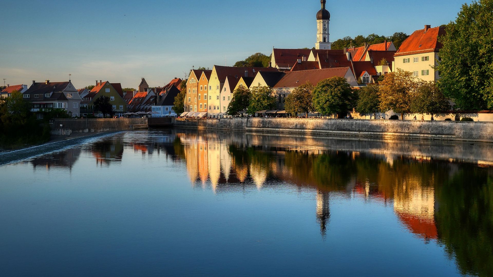 Blick auf eine Stadt mit bunten Häusern und einem Kirchturm, gelegen an einem ruhigen See bei blauem Himmel