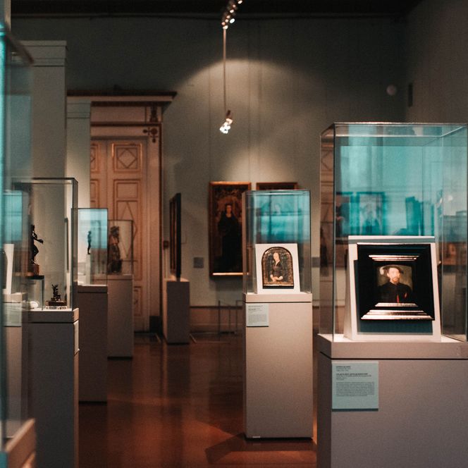 Raum in einem Museum mit mehreren Vitrinen und Gemälden