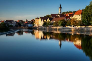 Blick auf eine Stadt mit bunten Häusern und einem Kirchturm, gelegen an einem ruhigen See bei blauem Himmel
