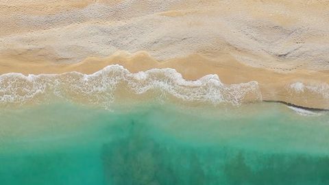 Türkis-farbene Wellen an einem Sandstrand aus Vogelperspektive