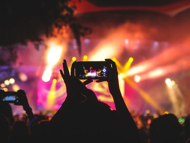 Person im Publikum bei einem Konzert filmt die beleuchtete Bühne mit Ihrem Smartphone