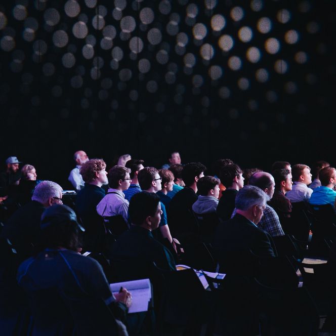 Publikum in mehreren Stuhlreihen bei einer Konferenz in einem dunklen Raum