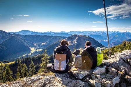 Familie mit zwei Kindern sitzt auf einem Berggipfel und schaut in den Horizont mit weiteren Bergen