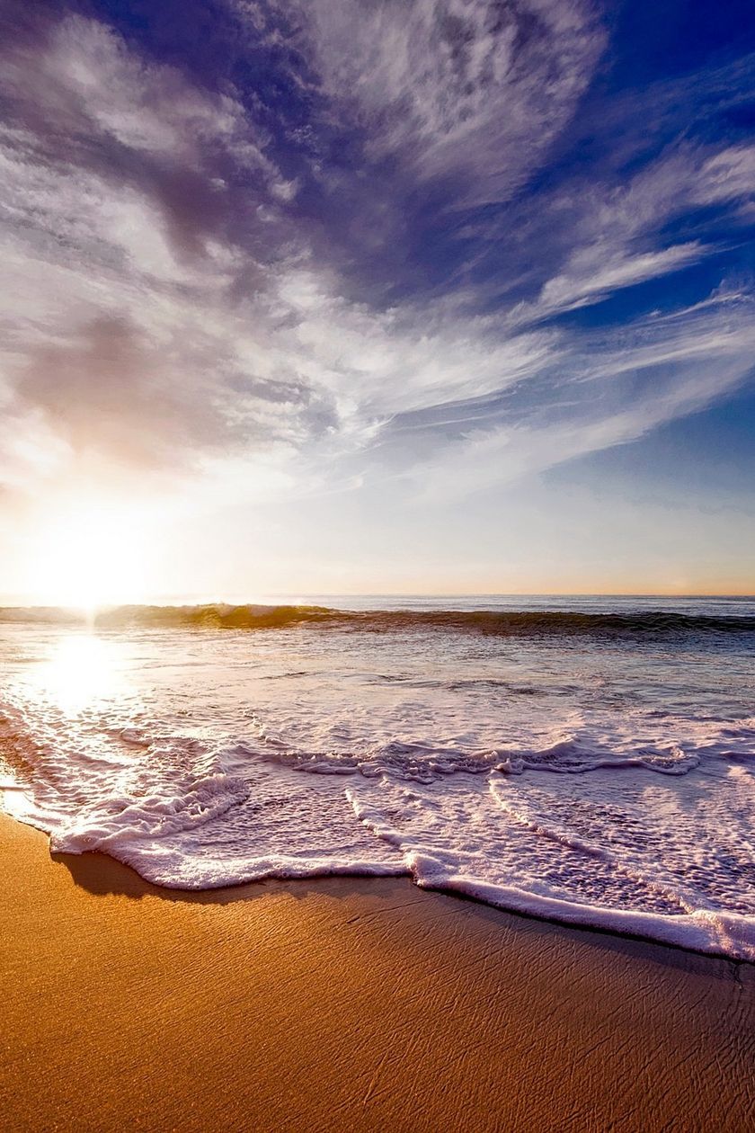 Sonnenuntergang über dem Meer mit Wellen, die an einen sandigen Strand rollen.