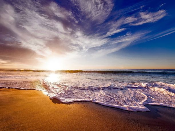 Sonnenuntergang am Meeresstrand Sonnenuntergang über dem Meer mit Wellen, die an einen sandigen Strand rollen.